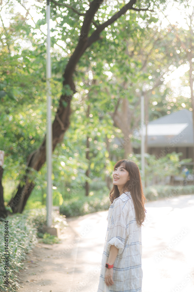 Asian woman enjoys summer day, breathing fresh air while walking through serene park surrounded by lush greenery and sunlight Asian woman enjoys summer day, breathing fresh air while walking through serene park surrounded by lush greenery and sunlight