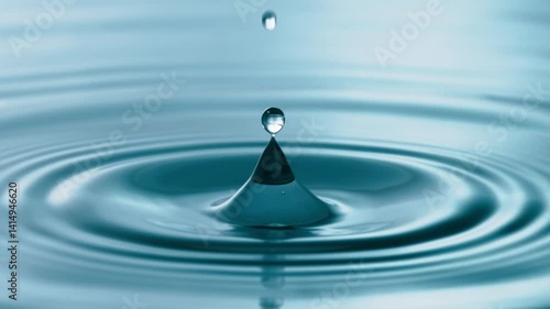 Closeup of water drops in slow motion. Droplets dripping with fascinating detail and making ripples on the blue liquid surface.
