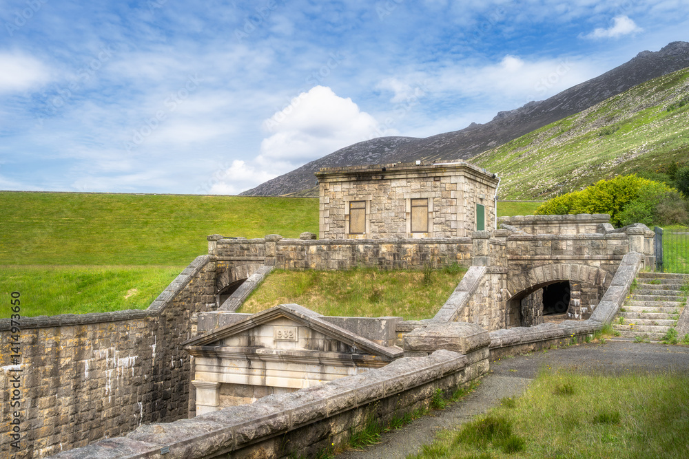 Silent Valley Reservoir stone structure dam stands among rolling green hills and a clear blue sky, creating a captivating scene that enchants with its timeless allure, Newry, Northern Ireland