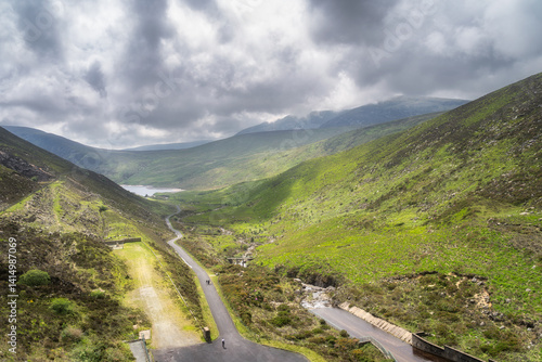 A stunning view of Silent Valley Reservoir, showcasing vibrant greenery, winding roads, and dramatic cloudy skies. Natures beauty unfolds in this serene landscape, Mourn Mountains, , Northern Ireland