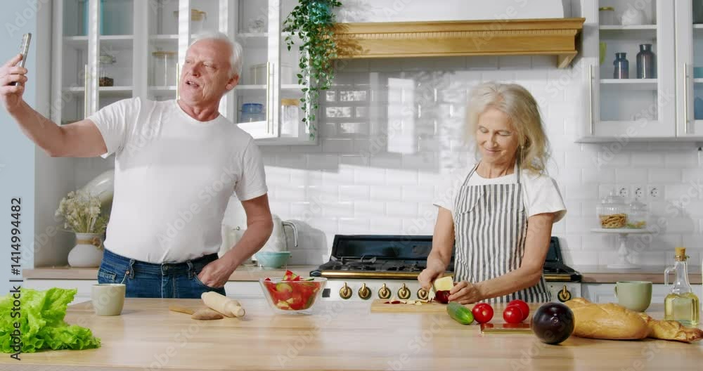 Aged people and modern technology, old man streaming from kitchen, wife cooking. Food bloggers filming trendy receipt of meal for vegetarians, happy mature spouses communicating online with followers Aged people and modern technology, old man streaming from kitchen, wife cooking. Food bloggers filming trendy receipt of meal for vegetarians, happy mature spouses communicating online with followers