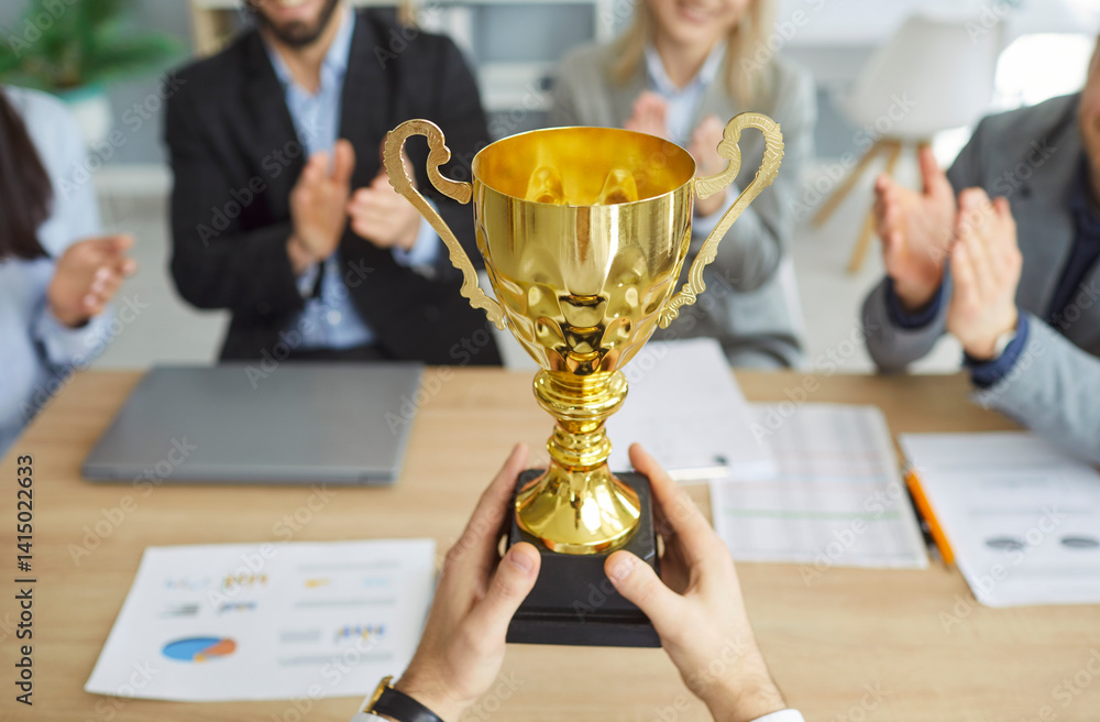 Male person winner holding the trophy award for success in business standing in office with a team of people colleagues applauding for company best employee reward. Success concept.