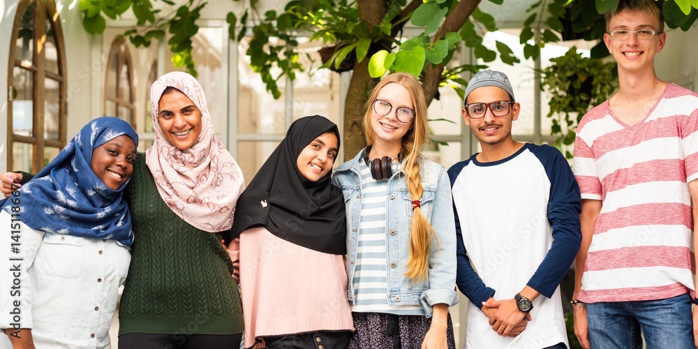 Group of diverse young adults smiling outdoors. Friends of various ethnicities enjoying time together. Happy, diverse, and friendly group portrait. Diverse young adult group in front of a house.