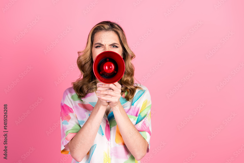 Fototapeta premium Young woman with a colorful shirt holding a red megaphone and expressing emotions against a vibrant pink background
