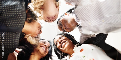 Diverse group of women, African American and Caucasian, smiling and looking down in a circle. Group of friends, team, or colleagues bonding. Diverse group unity. Business women team working together