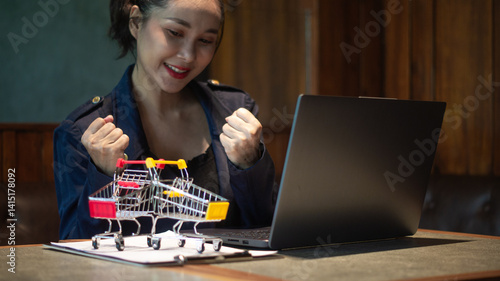 Wallpaper Mural Businesswoman smiling and gesturing happily at successful online deal closing via laptop and shopping cart conveying trade. Torontodigital.ca