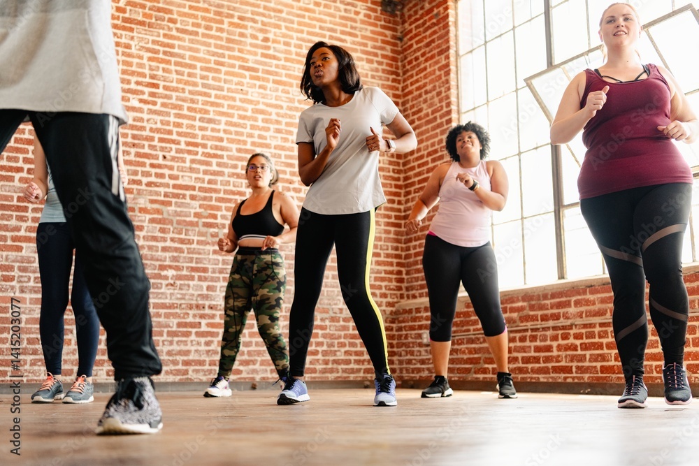 Fototapeta premium Group fitness class with diverse women exercising. Women in workout attire, fitness focus, diverse group. Women enjoying fitness in a bright studio. Diverse people exercising in fitness class.