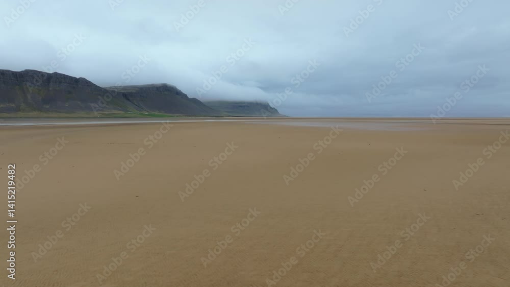 Low tide at Raudasandur beach in Iceland, revealing golden sands and shallow water channels under a cloudy sky with mountains in the background. Low tide at Raudasandur beach in Iceland, revealing golden sands and shallow water channels under a cloudy sky with mountains in the background.