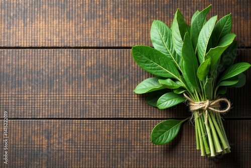 A vibrant bunch of fresh green leaves tied with twine, resting on a dark brown wooden surface