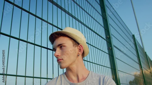 Wallpaper Mural Portrait of a man wearing a hat, standing near a metal fence on a sunny day, camera tracking Torontodigital.ca