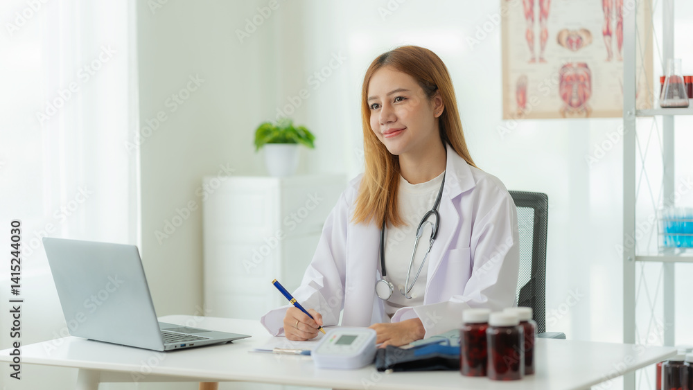 Smiling Asian female doctor in lab coat and stethoscope sitting next to online consultation table in doctor's office Smiling Asian female doctor in lab coat and stethoscope sitting next to online consultation table in doctor's office
