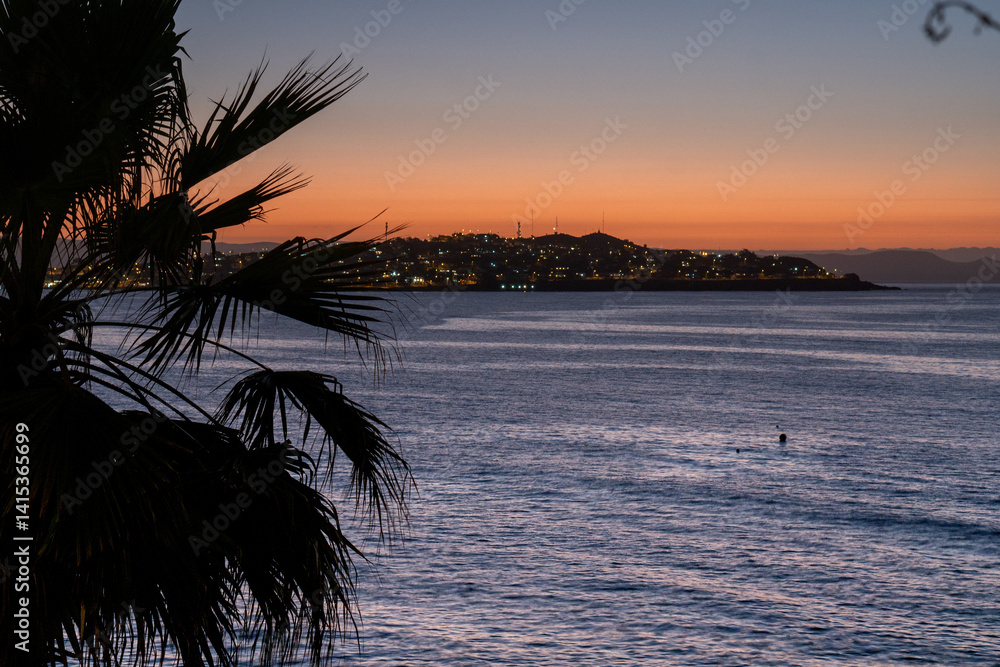 City lights of Tongoy begin to glow as the sun sets over the Pacific coast, casting a warm hue on the tranquil townscape. Tongoy, Chile