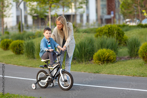 Father teaching son riding bike on the bike path. Father helping excited son to ride a bicycle in modern urban district. Child learning to ride cycle with his dad. Fathers day.