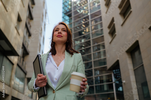 Fotografia Confident businesswoman walking down the street, holding a laptop and a coffee,