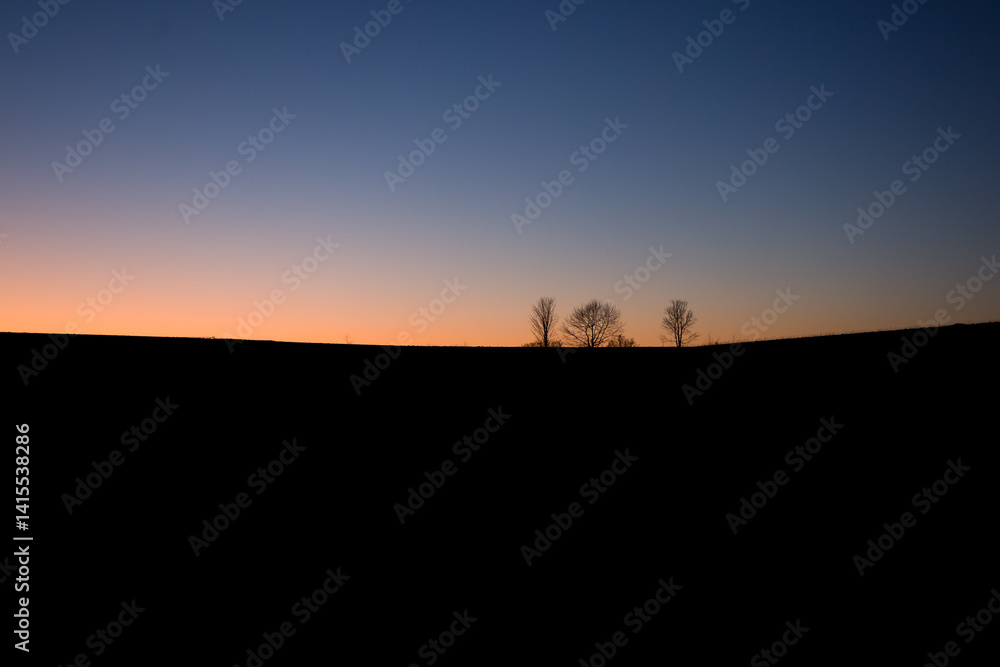 sunset at the blue hour with dark foreground and small trees as shilouette in an orange blue multicolored sky sunset at the blue hour with dark foreground and small trees as shilouette in an orange blue multicolored sky