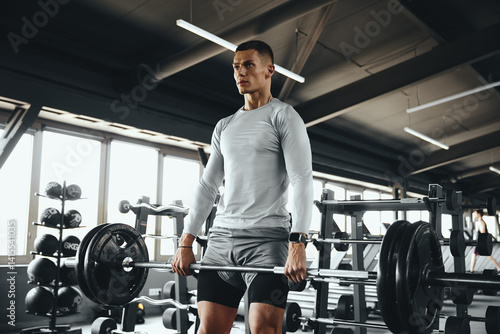 Athletic man doing a deadlift with a barbell in a modern gym. Focused strength training surrounded by fitness equipment and natural light