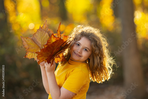 Child portrait in autumn fall park. Little child in autumn orange leaves, outdoor portrait. Cute child face with autumn leaves in autumn park. Child hold falling leaves. Outdoor portrait of kids.