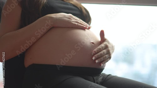 A close-up of a pregnant woman gently caressing her bare belly. A peaceful, emotional moment symbolizing love, motherhood, and the baby soon to arrive.