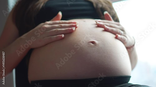 A pregnant woman lovingly caresses her bare belly from the front, her hands gently embracing her growing baby bump. A serene moment of anticipation, love, and maternal connection.