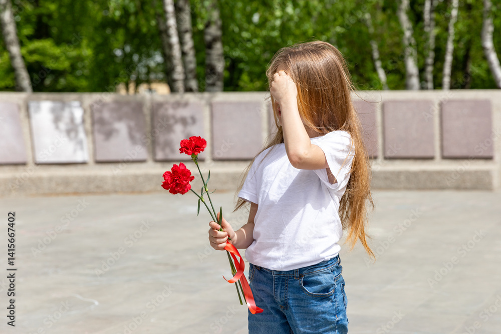Victory Day. Little Girl with red carnations at the Eternal flame near the monument of Unknown soldiers tomb. Patriotic education at school.