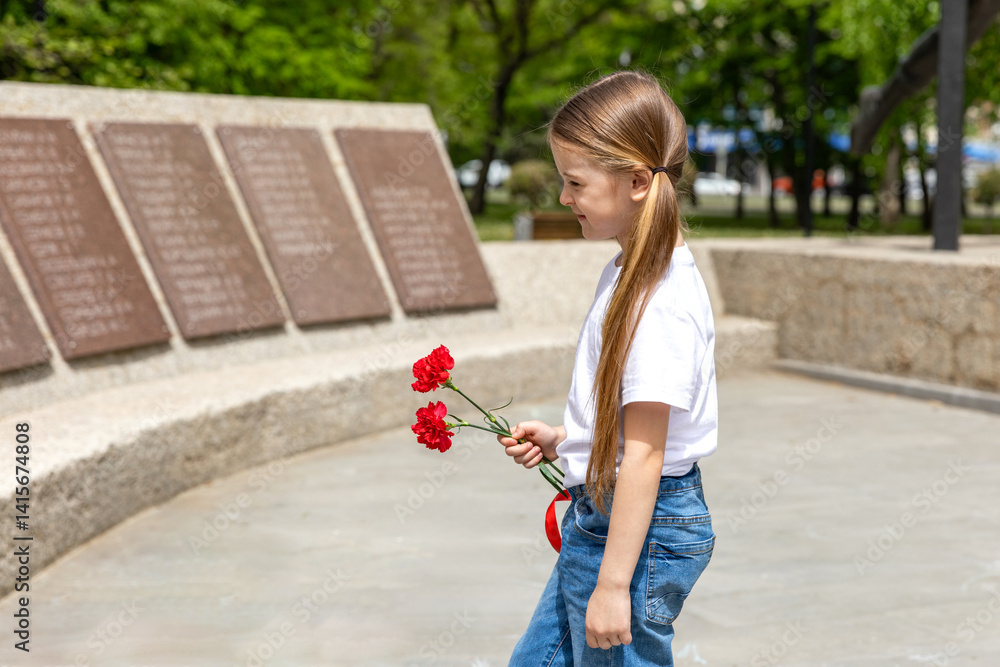 Victory Day. Little Girl with red carnations at the Eternal flame near the monument of Unknown soldiers tomb. Patriotic education at school.