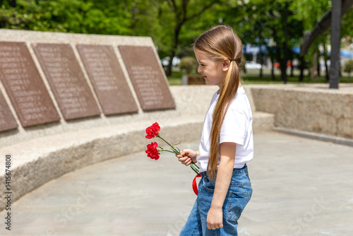 Obraz na płótnie Victory Day. Little Girl with red carnations at the Eternal flame near the monument of Unknown soldiers tomb. Patriotic education at school. w salonie