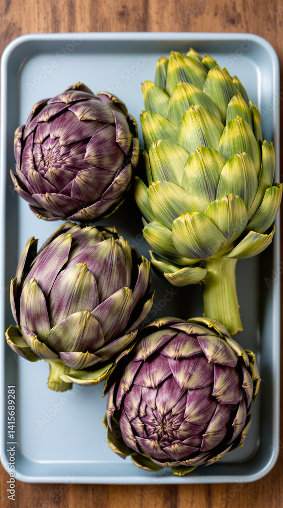 Fototapeta premium four artichokes two purple and two green arranged in a pale blue tray