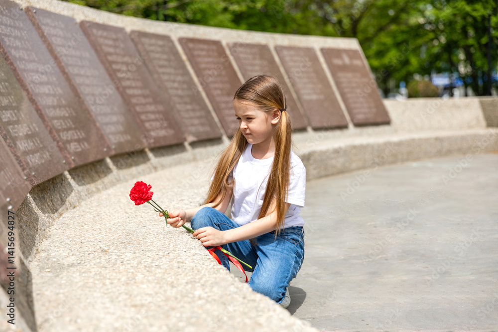 The memory of soldiers in Great Patriotic War. Little girl laying red carnations at the monument to fallen soldiers in world War II. Victory Day on May 9.
