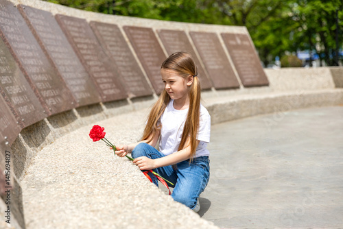 Obraz na płótnie The memory of soldiers in Great Patriotic War. Little girl laying red carnations at the monument to fallen soldiers in world War II. Victory Day on May 9. w salonie
