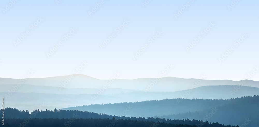 Fototapeta premium Layered Blue Mountain Ranges in Morning Haze Over Water.