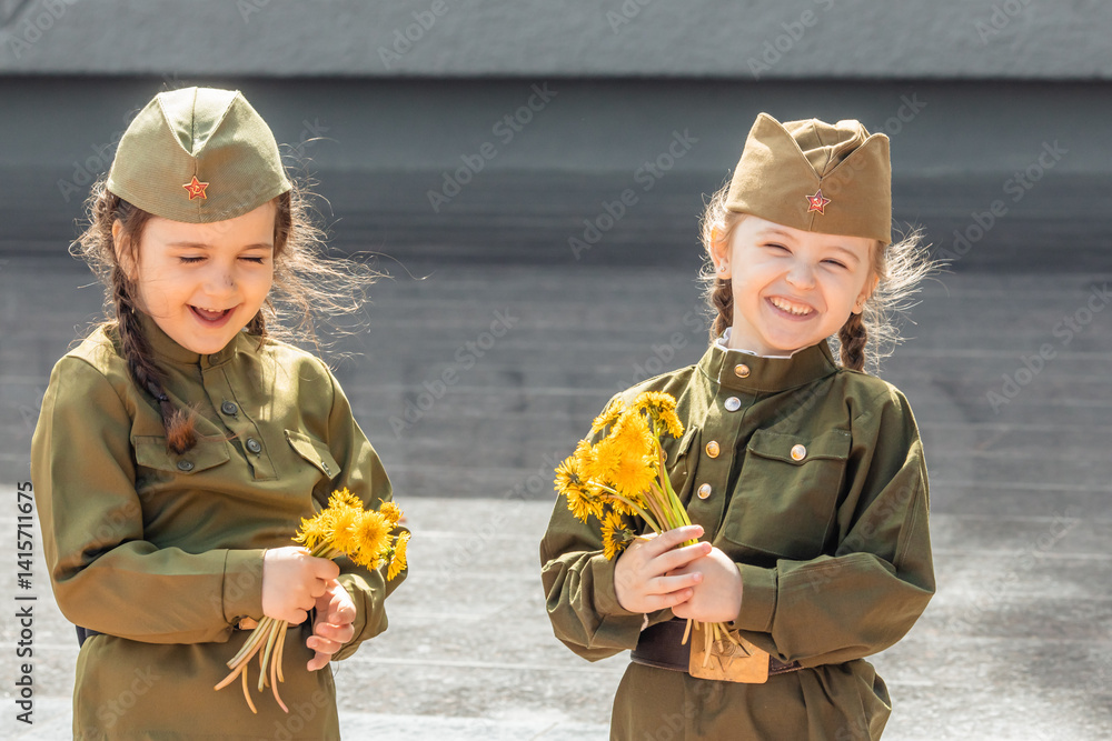 Patriotic education of children. Little girls with long braids in a military uniform, military cap, hold flowers in hands against the background of the memorial. Photo for the Victory Day on May 9