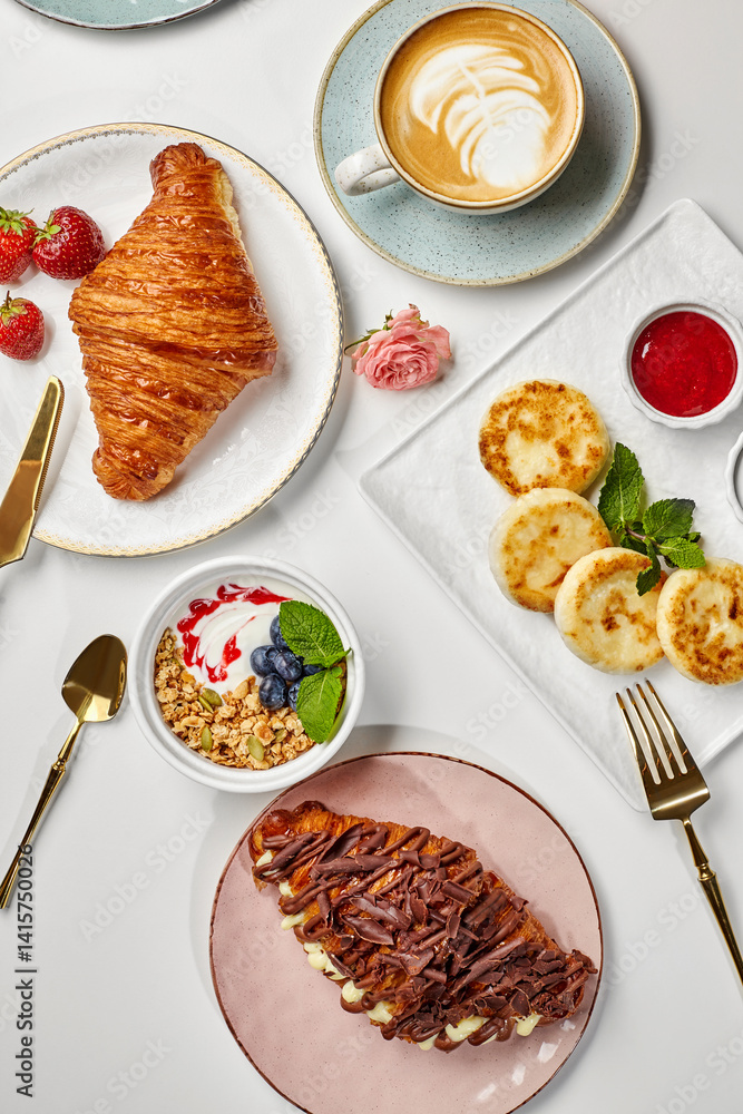Delicious breakfast with croissants, pancakes, granola, cappuccino and berries served on white table