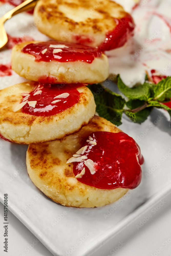 Cottage cheese pancakes, syrniki, with raspberry jam, mint and almond flakes on white plate