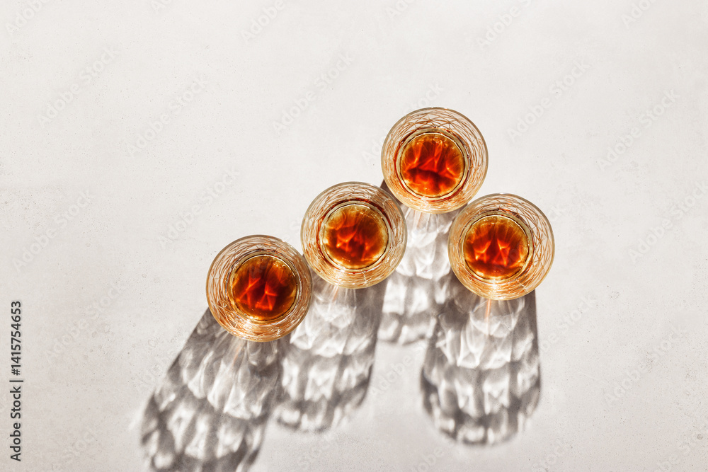 Transparent alcohol Glasses with dark shadows at sunlight on beige table, top view minimal style, aesthetic flat lay shiny glass sparkling at natural light, summer strong drink, luxury lifestyle