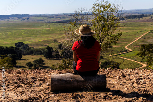 Obraz na płótnie Woman sitting on a wooden stump looks out over the landscape of rural roads and farmland from a mountain range in Brazil w salonie
