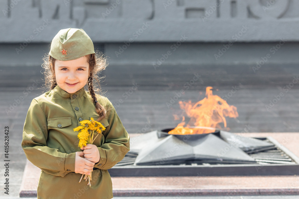 Patriotic education of children. Little girl with long braids in a military uniform, military cap, holds flowers in hands against the background of the memorial. Photo for the Victory Day on May 9