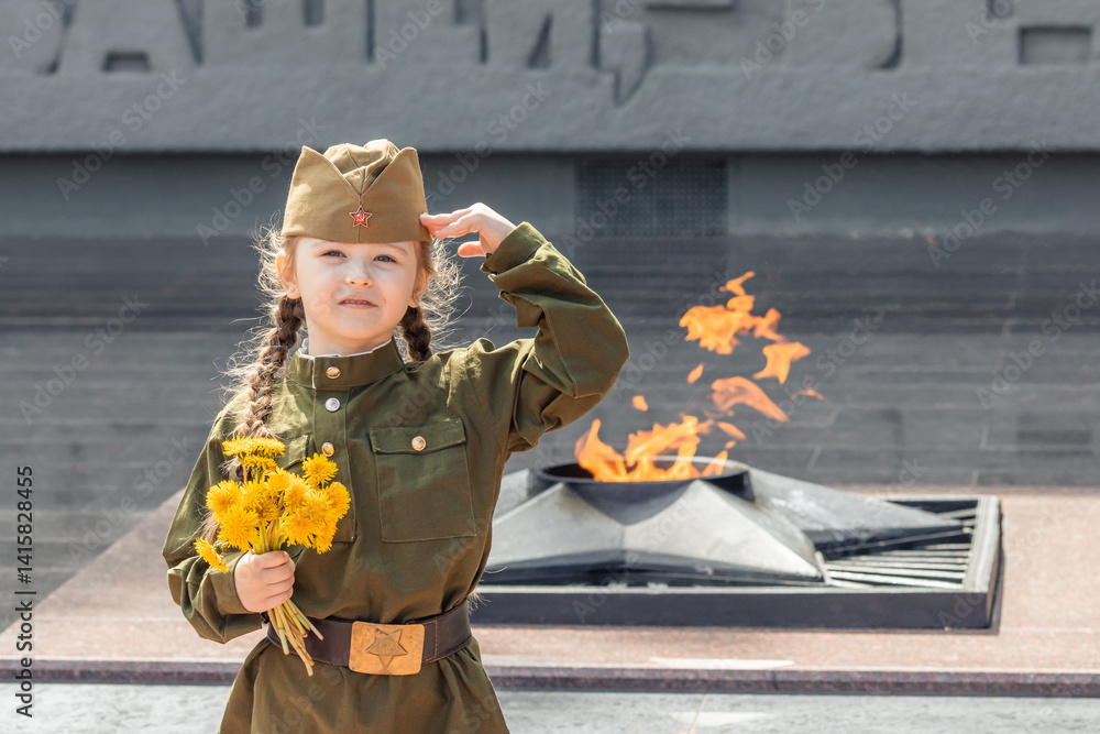 Patriotic education of children. Little girl with long braids in a military uniform, military cap, holds flowers in hands against the background of the memorial. Photo for the Victory Day on May 9