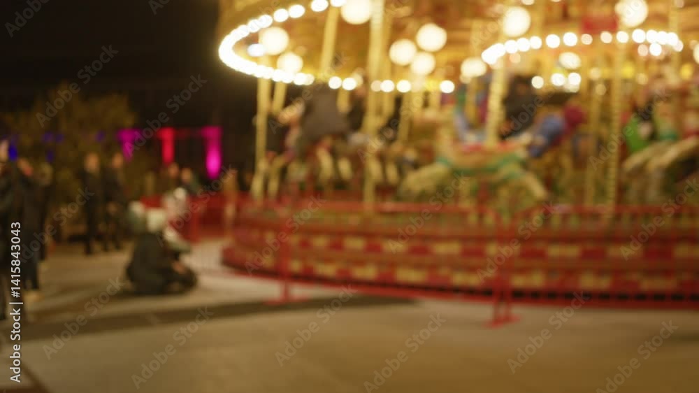 Blurred night view of carousel with people and bright lights in a park setting, featuring defocused bokeh and a festive atmosphere. Blurred night view of carousel with people and bright lights in a park setting, featuring defocused bokeh and a festive atmosphere.