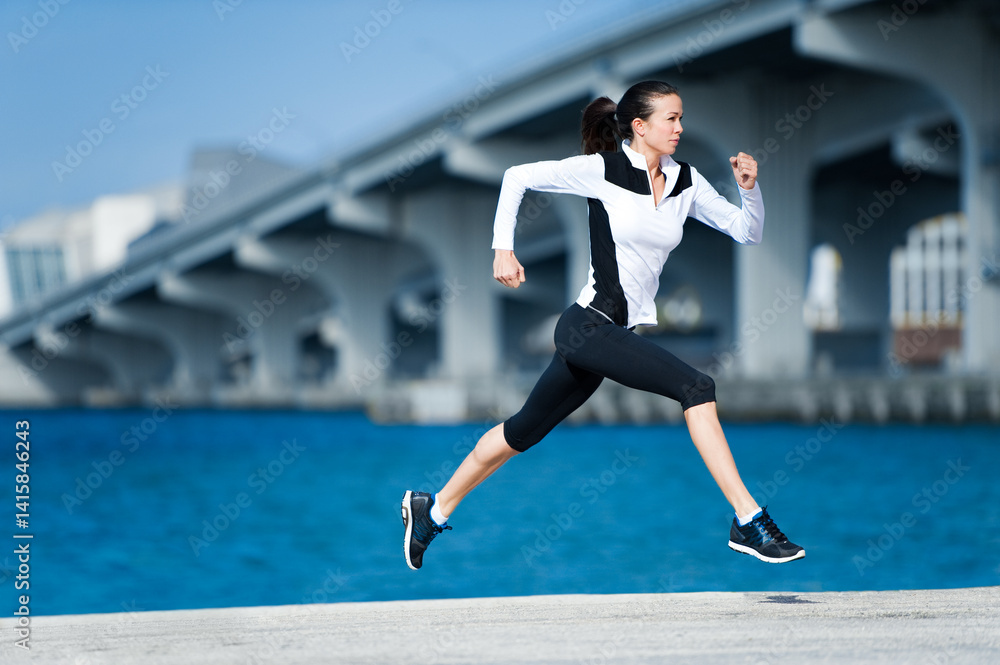 Fototapeta premium Young woman running jogging by Biscayne Bay Miami Florida with causeway bridge in background