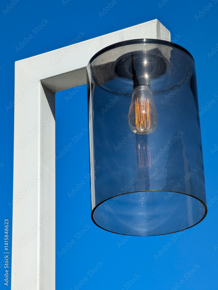 Modern lamp with glass shade against clear blue sky.