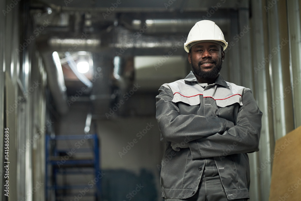 Low angle portrait of young African American builder with crossed hands posing for photo at construction site Low angle portrait of young African American builder with crossed hands posing for photo at construction site