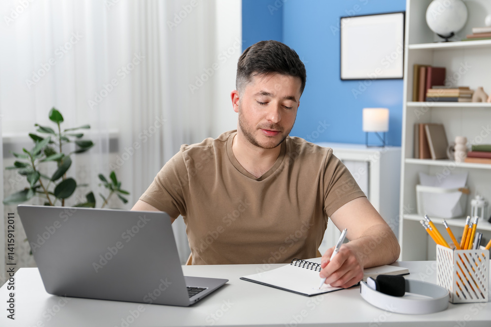 Man taking notes during online lesson at desk indoors. Self-study Man taking notes during online lesson at desk indoors. Self-study