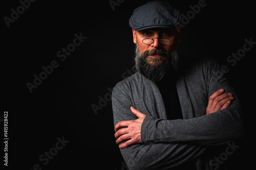 Obraz na płótnie Close-up portrait of a serious bearded man in flat cap and glasses on black background. Stylish, intense look with confident and mysterious expression w salonie