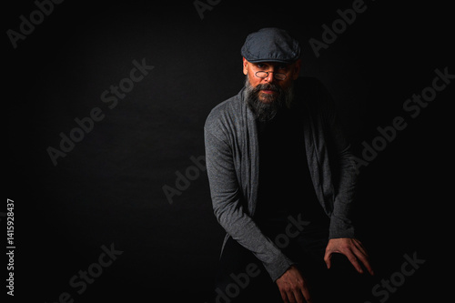 Obraz na płótnie Close-up portrait of a serious bearded man in flat cap and glasses on black background. Stylish, intense look with confident and mysterious expression w salonie