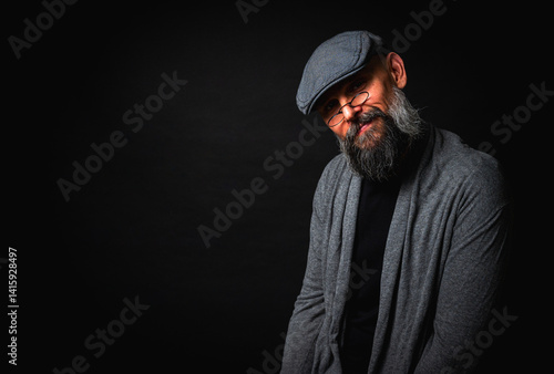 Close-up portrait of a serious bearded man in flat cap and glasses on black background. Stylish, intense look with confident and mysterious expression