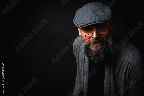 Obraz na płótnie emotional, macro portrait of a serious bearded man in a cap and glasses on a black background. Stylish, intense look with a confident and mysterious expression, emotions place for inscription on a bil w salonie