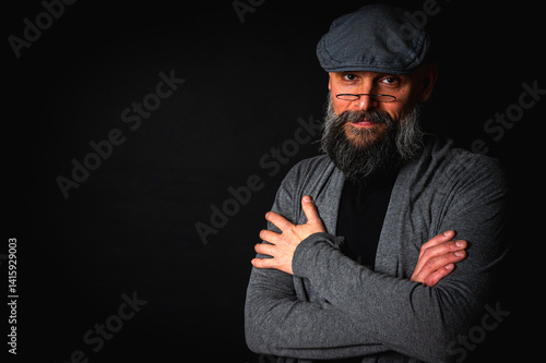 Obraz na płótnie Close-up portrait of a serious bearded man in flat cap and glasses on black background. Stylish, intense look with confident and mysterious expression w salonie