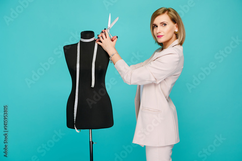 Quadro su tela fashion designer woman holding scissors near mannequin with measuring tape on turquoise background