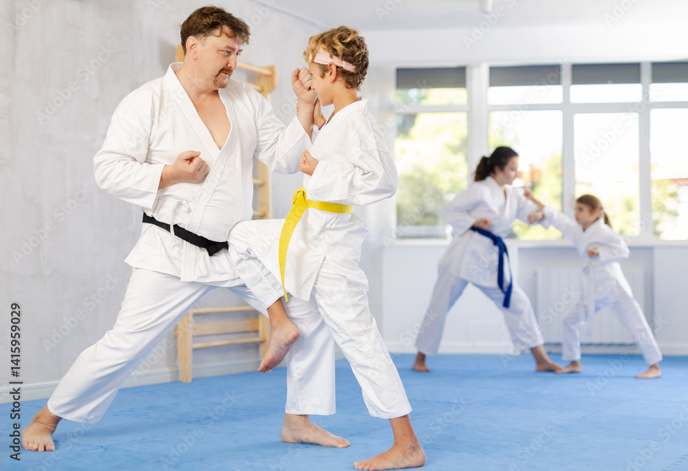 Father and son karatekas in kimonos practice karate fighting in studio Father and son karatekas in kimonos practice karate fighting in studio