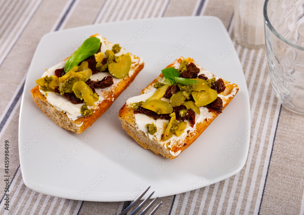 Healthy sandwiches for breakfast or lunch with toasted baguette, cream cheese spread, slices of sun-dried tomatoes, green olives and pesto. Mediterranean style vegetarian appetizers Healthy sandwiches for breakfast or lunch with toasted baguette, cream cheese spread, slices of sun-dried tomatoes, green olives and pesto. Mediterranean style vegetarian appetizers